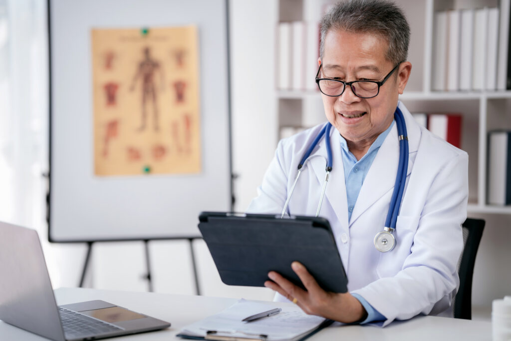 Senior male doctor with stethoscope is working on laptop and sea